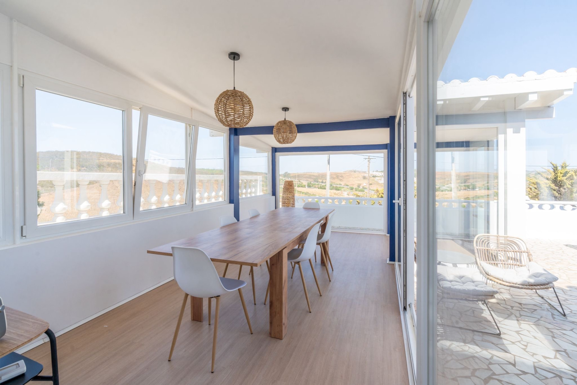 Long wooden dining table in a light-filled glazed room with countryside views