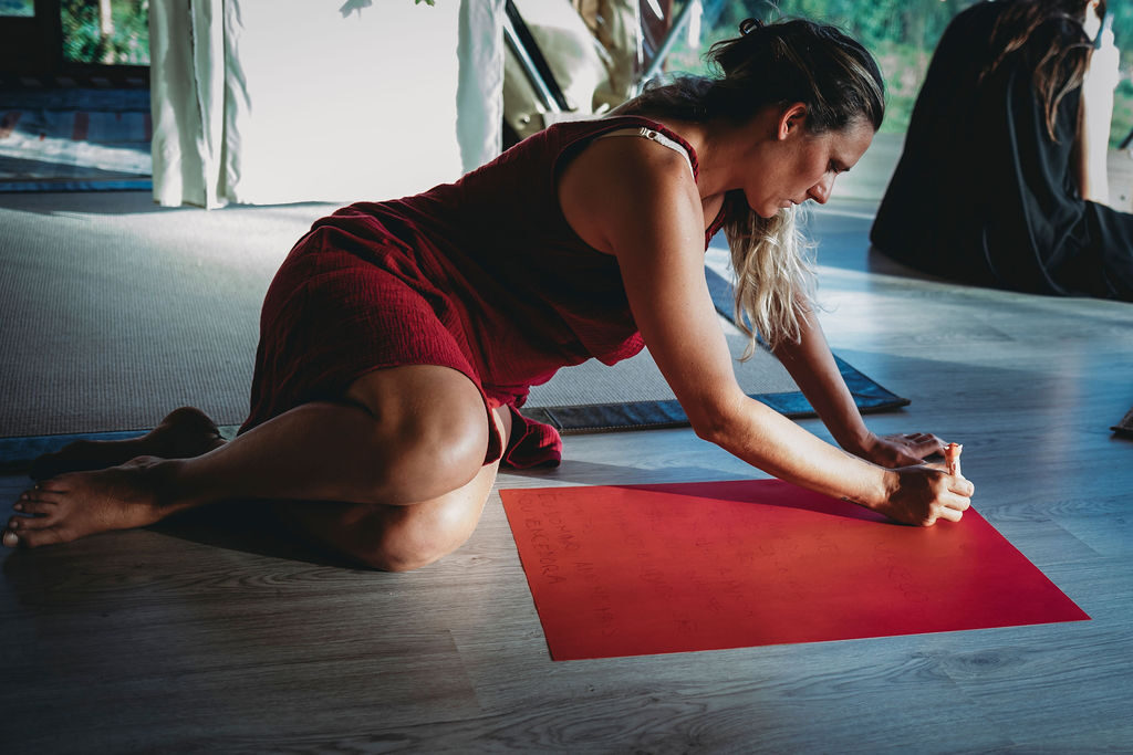 A woman in expressive movement on the studio floor, reaching along a red mat