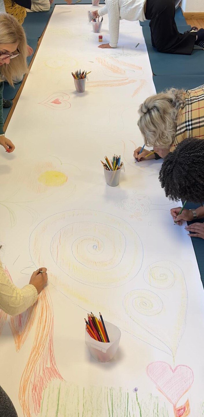 Hands drawing together in colour on a long sheet of paper during a group session